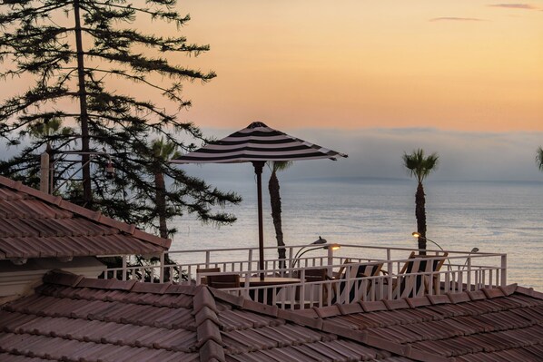 A seaside terrace with a striped umbrella, wooden chairs, and a view of the ocean. - Villa Barranco by Ananay Hotels (Lima)