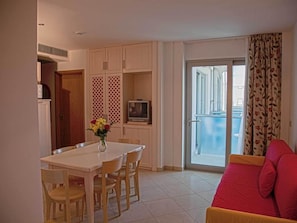 Un coin repas avec une table et des chaises, un téléviseur posé sur un meuble, et un balcon avec vue.