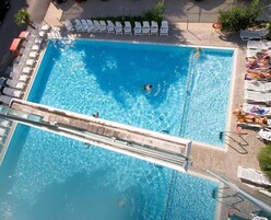 Una piscina rettangolare con trampolino, circondata da lettini e ombrelloni.