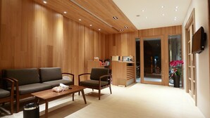 Un intérieur moderne avec un mur recouvert de panneaux en bois, un canapé, deux fauteuils, une petite table et un téléviseur fixé au mur.