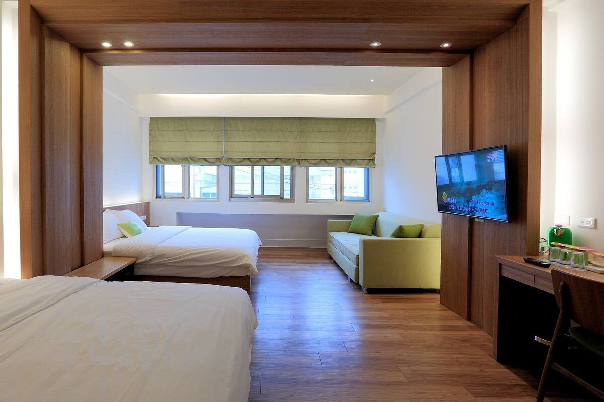 A hotel room with two beds, a sofa, a TV, and a desk.