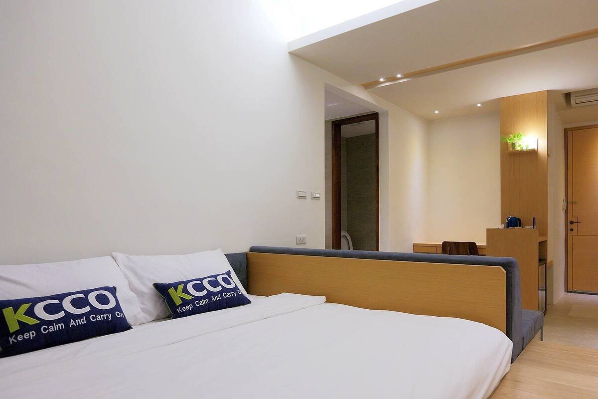 A modern hotel room with a bed, a desk, and a bathroom visible through an open door.