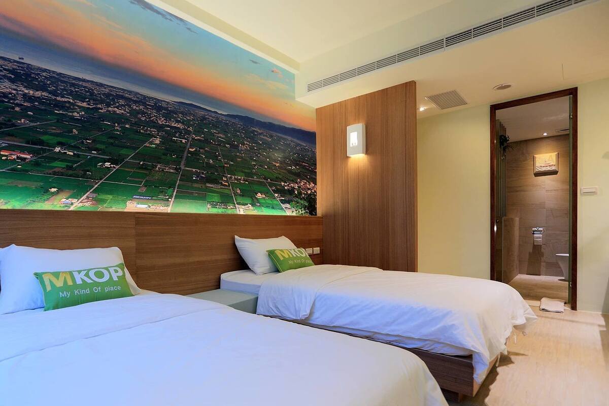 A hotel room with two beds, a mural of a landscape, and a wooden headboard.
