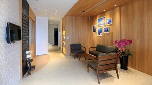 Un espace d’accueil avec un mur en bois, un téléviseur, un comptoir de réception et un coin salon avec des chaises et un canapé.