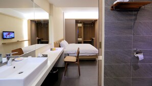 Une chambre d’hôtel moderne dotée d’un grand miroir, d’un lit, d’une coiffeuse avec un lavabo et d’un espace douche.