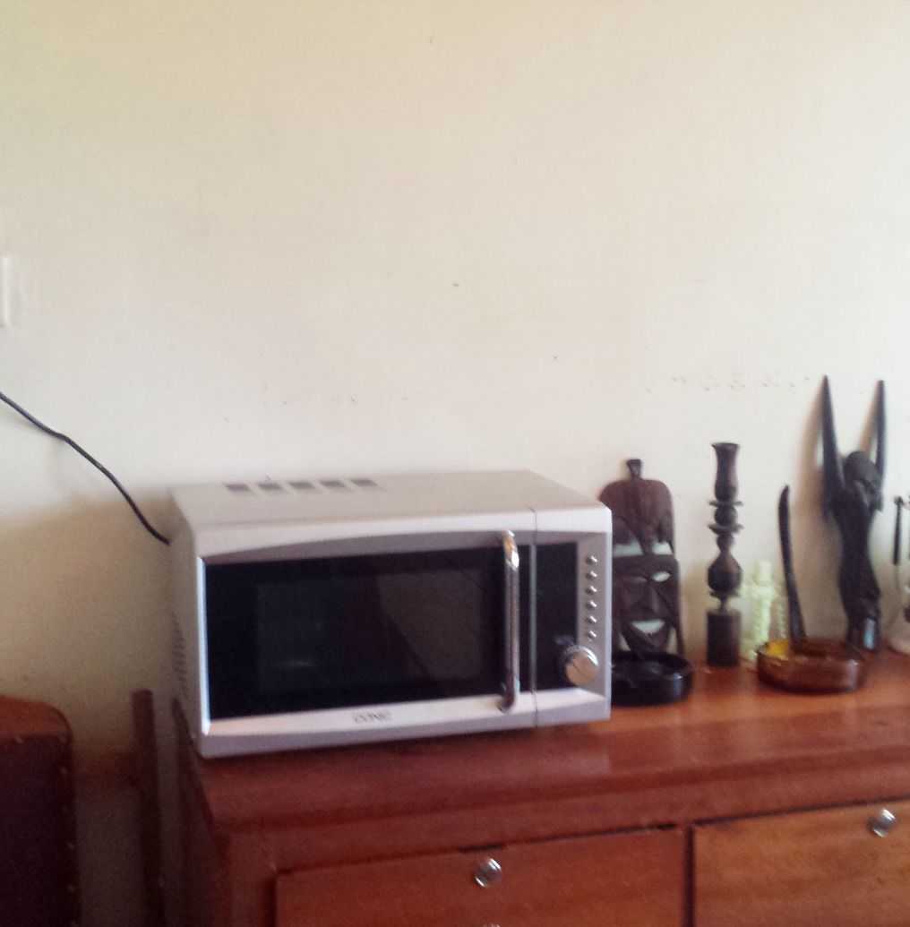 Un microondas blanco sobre un mueble de madera, con un enchufe fijado a la pared al fondo.