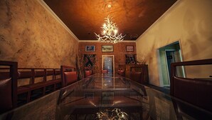 Un espace repas comprenant une longue table, des chaises, un lustre et un mur en briques orné de tableaux encadrés.