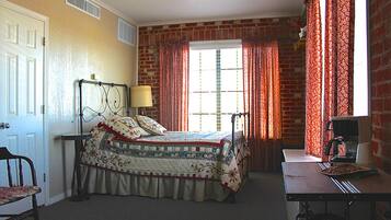 A bedroom with a bed, a desk, and a chair. There is a window with curtains and a brick wall.
