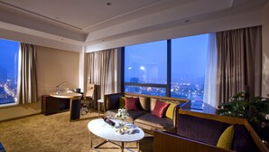 A modern hotel room with a large window, a sofa, a coffee table, and a desk with a chair. - Shuguang International Hotel Huaian (Huai'an)