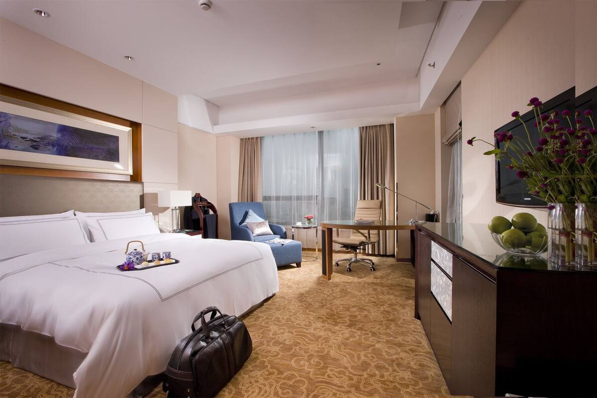 A hotel room with a large bed, a desk, a chair, a television, and a vase with flowers.
