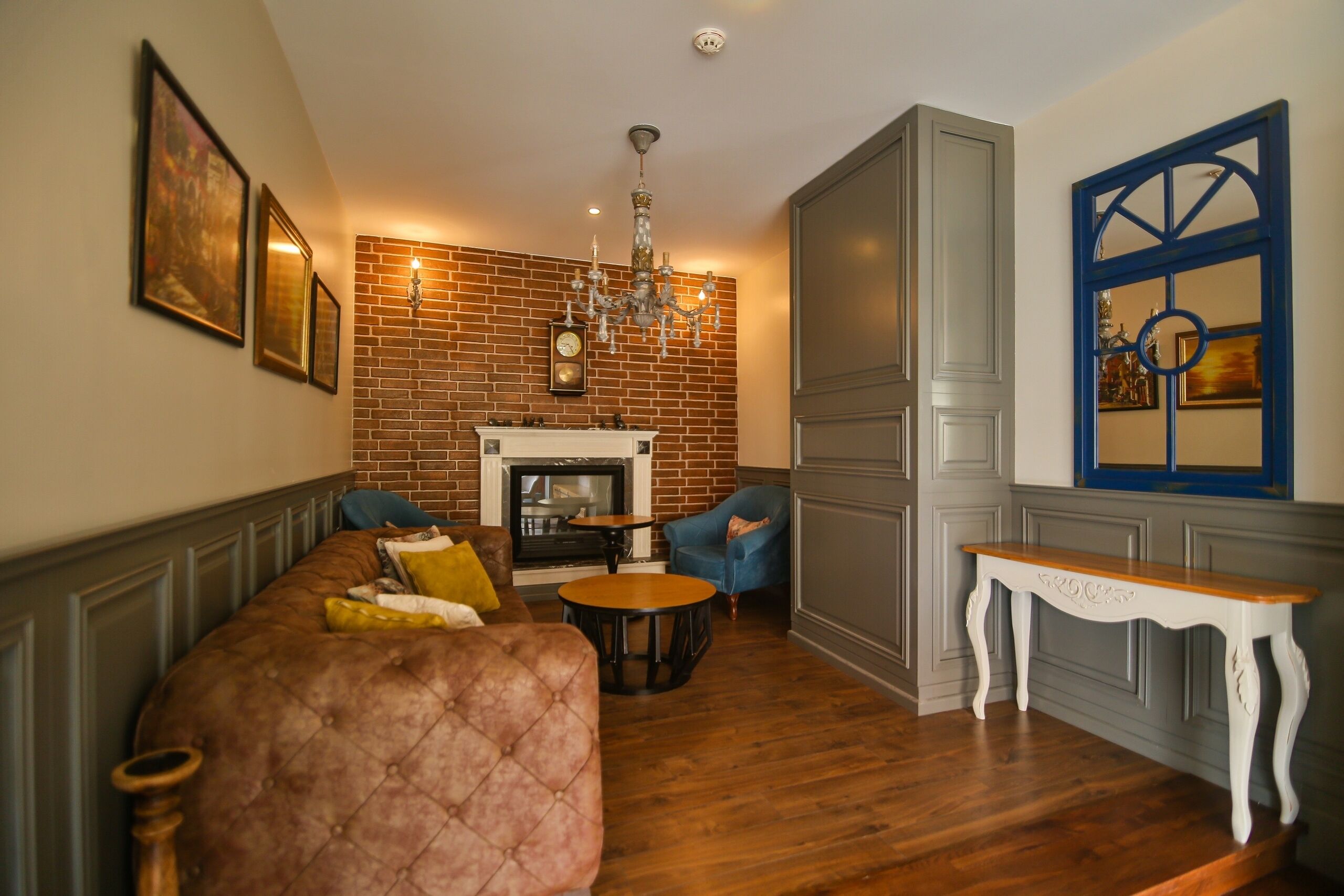 Un salón con pared de ladrillo, chimenea, candelabro, un sillón azul y una mesa de madera.