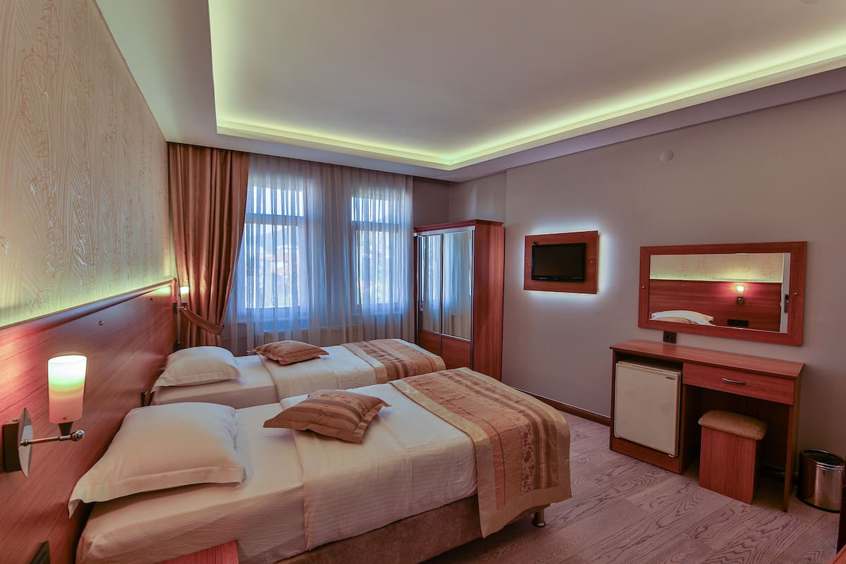 A hotel room with two beds, a desk, a mirror, a TV, and a small refrigerator.