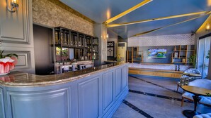 A bar area with a marble countertop, shelves with glasses, and a television on the wall. - Seymen Hotel (Amasra)