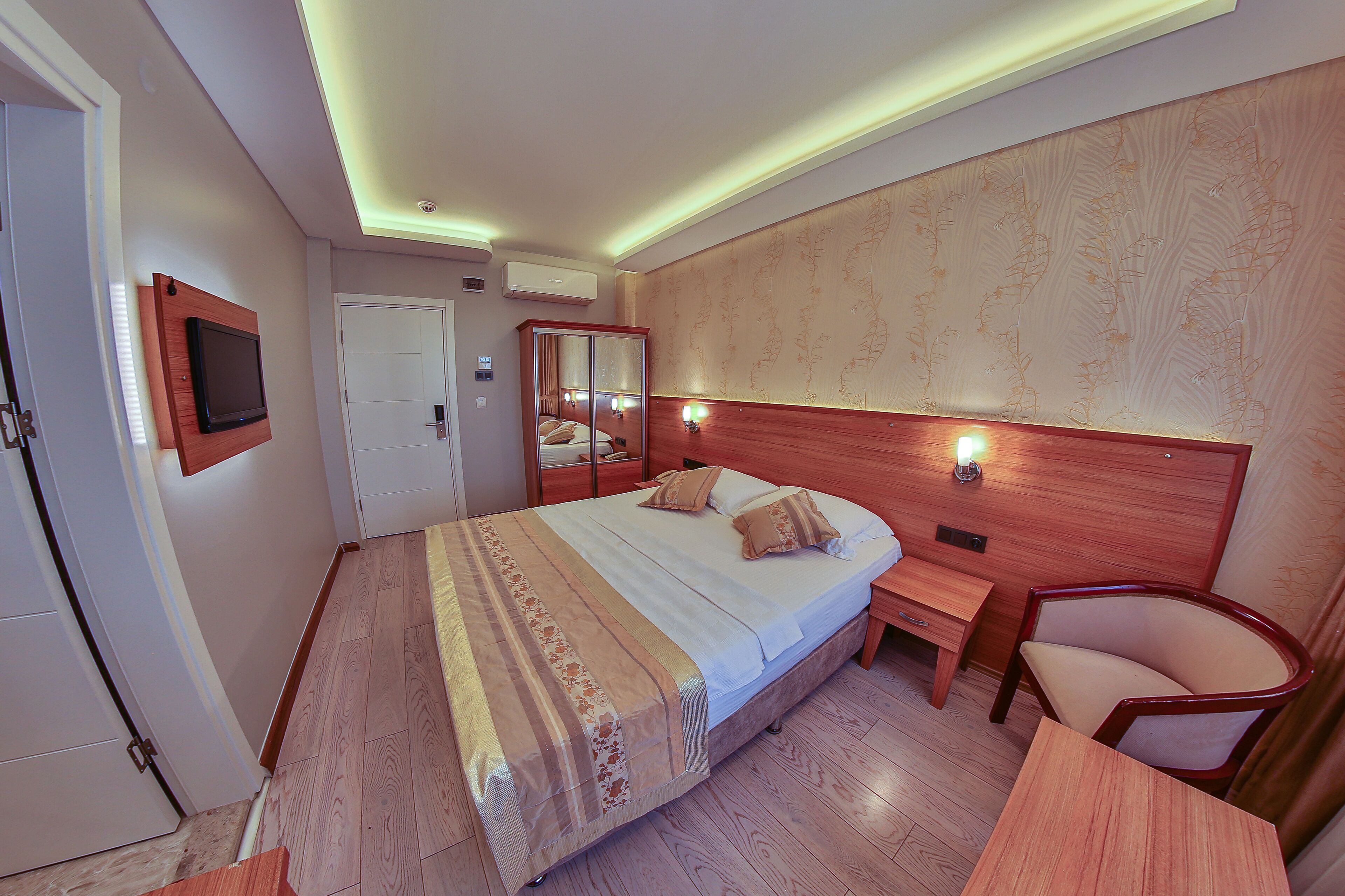A hotel room with a bed, bedside table, chair, and a TV mounted on the wall.