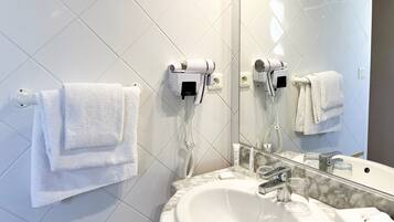 A modern bathroom with a white sink, a mirror, and two hair dryers mounted on the wall.