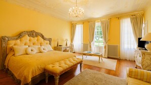Een ruime slaapkamer met een groot bed, een kroonluchter en uitzicht op het omliggende landschap.