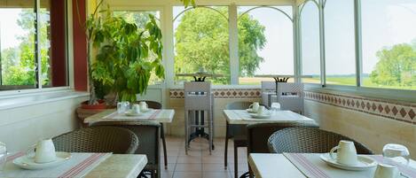A covered patio with tables and chairs, potted plants, and a view of the outdoors.