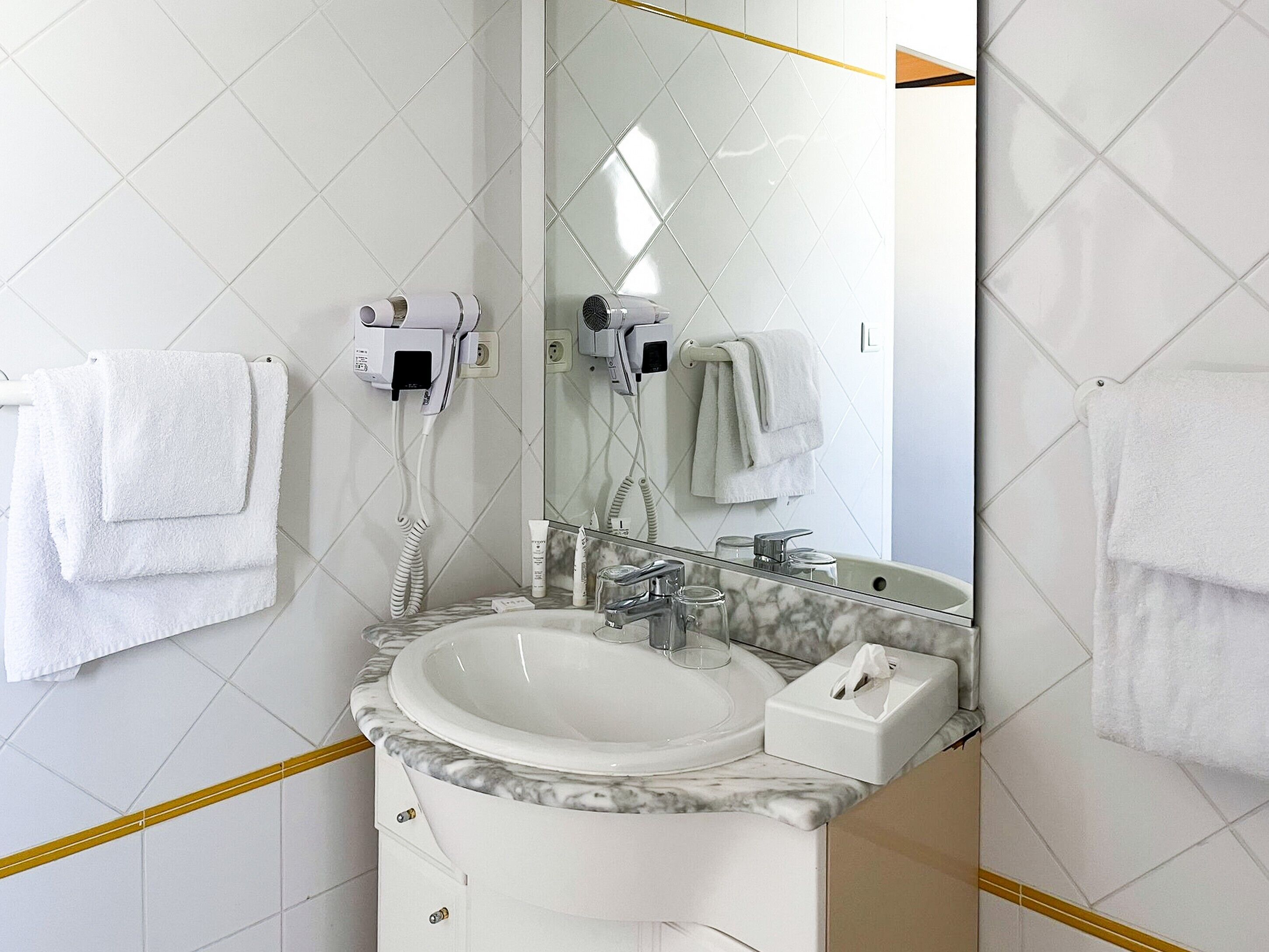 A bathroom with a white sink, a mirror, and two hair dryers mounted on the wall.