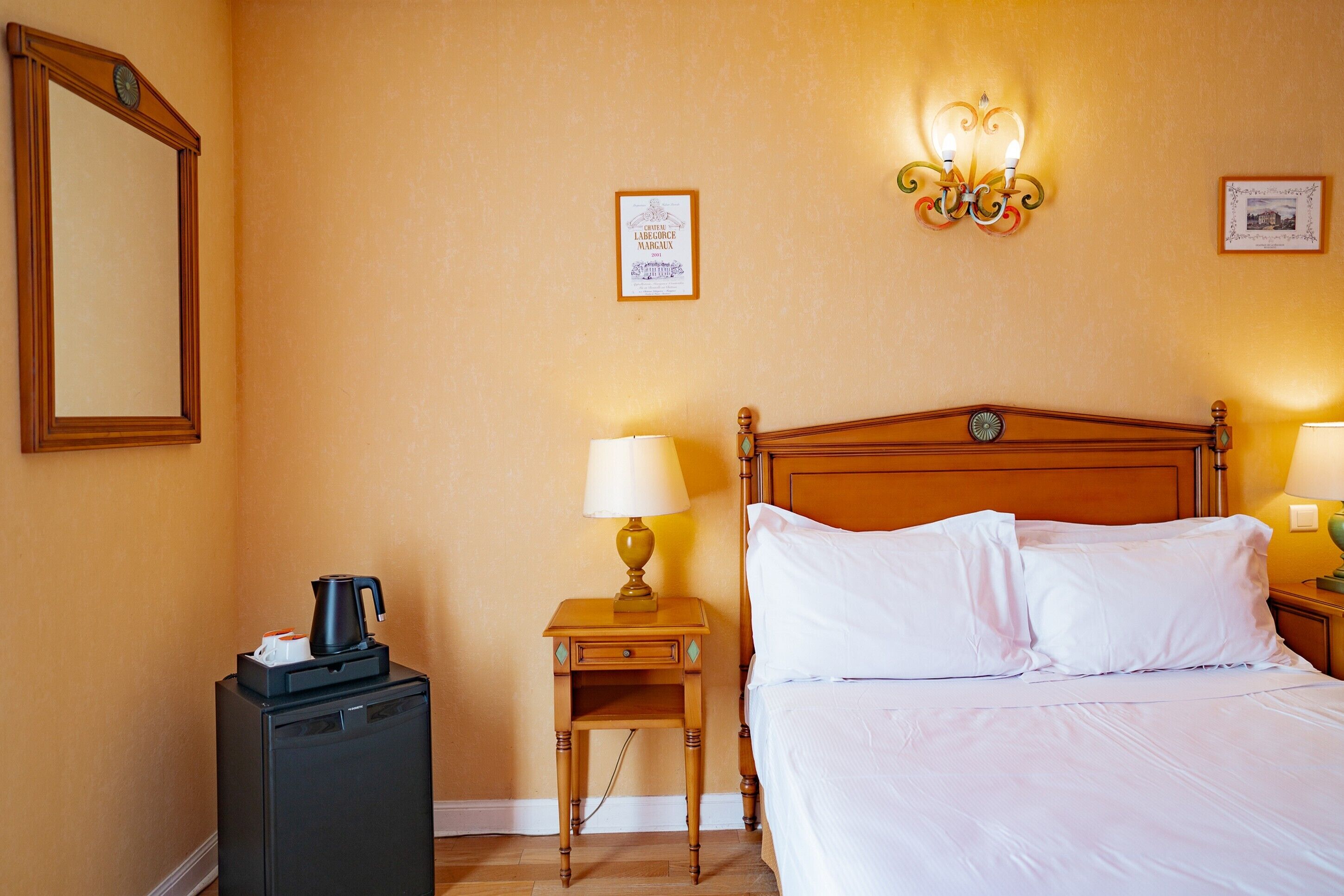 Une chambre d’hôtel comprenant un lit, des lampes de chevet, une table de chevet avec une lampe, une petite table avec une bouilloire et un réfrigérateur.