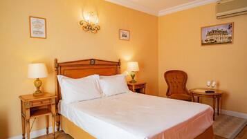 A hotel room with a large bed, two bedside tables with lamps, a chair, and a small table with two wine glasses.