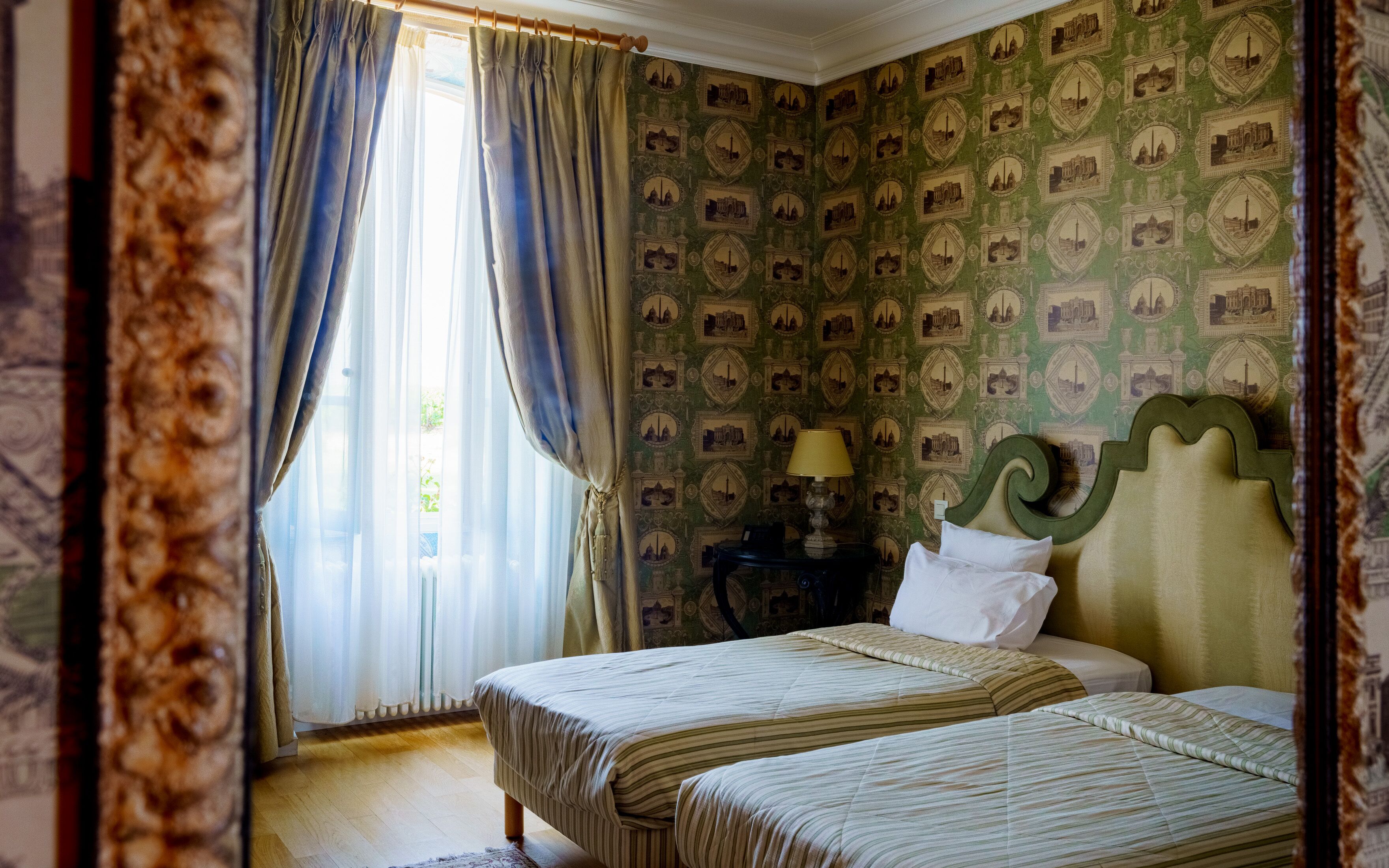 Een kamer met twee bedden, een nachtkastje, een lamp en een raam met gordijnen.