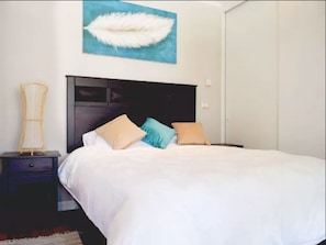 A bedroom with a bed, a nightstand, a lamp, and a painting on the wall. - AlojaRent Da Vinci (Santiago)
