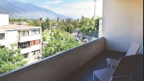 Ein Balkon mit Blick auf eine Stadtlandschaft und Berge. Zwei Stühle und ein Tisch befinden sich auf dem Balkon.