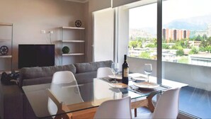 Ein modernes Wohnzimmer mit einem Glastisch, einem grauen Sofa und einem großen Fenster mit Blick auf die Stadt.