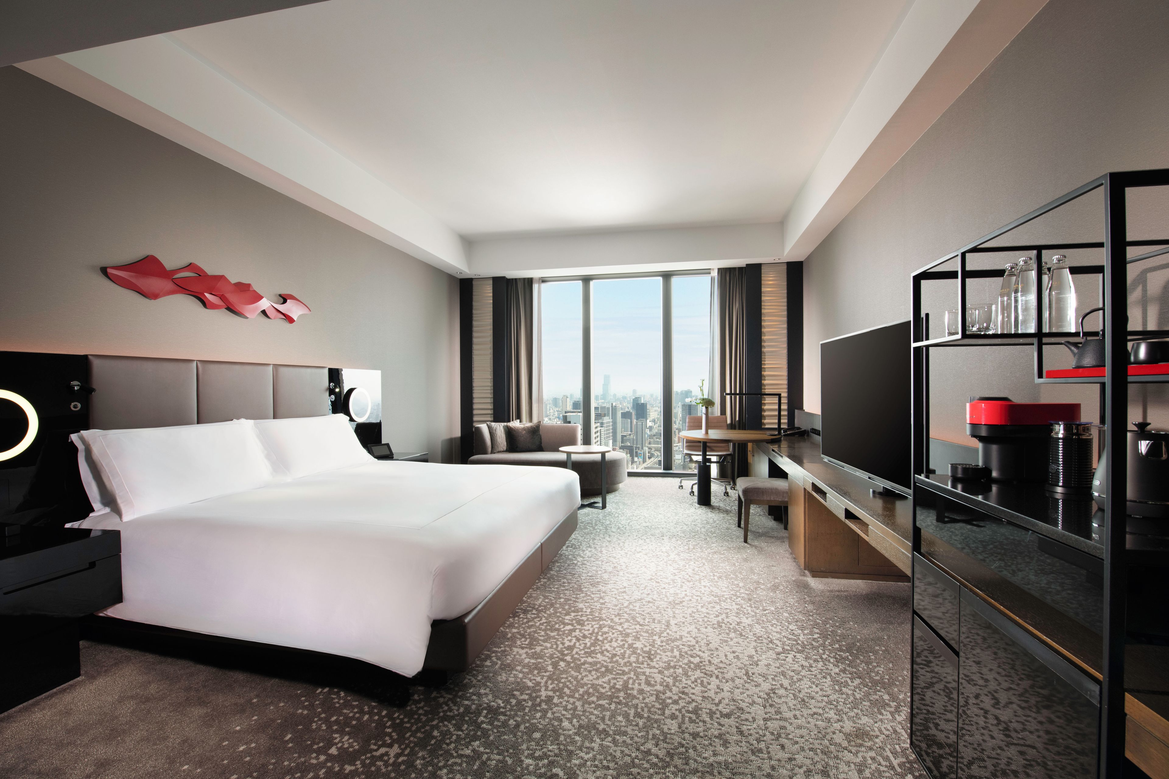 A hotel room with a large bed, a desk, a television, and a view of the city.