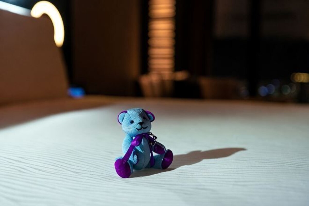 Un petit ours en peluche bleu est assis sur un lit.