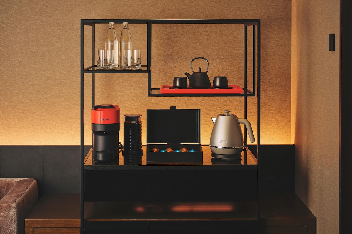 A modern kitchen with a coffee maker, kettle, and tea set on a black shelf unit against a textured wall.