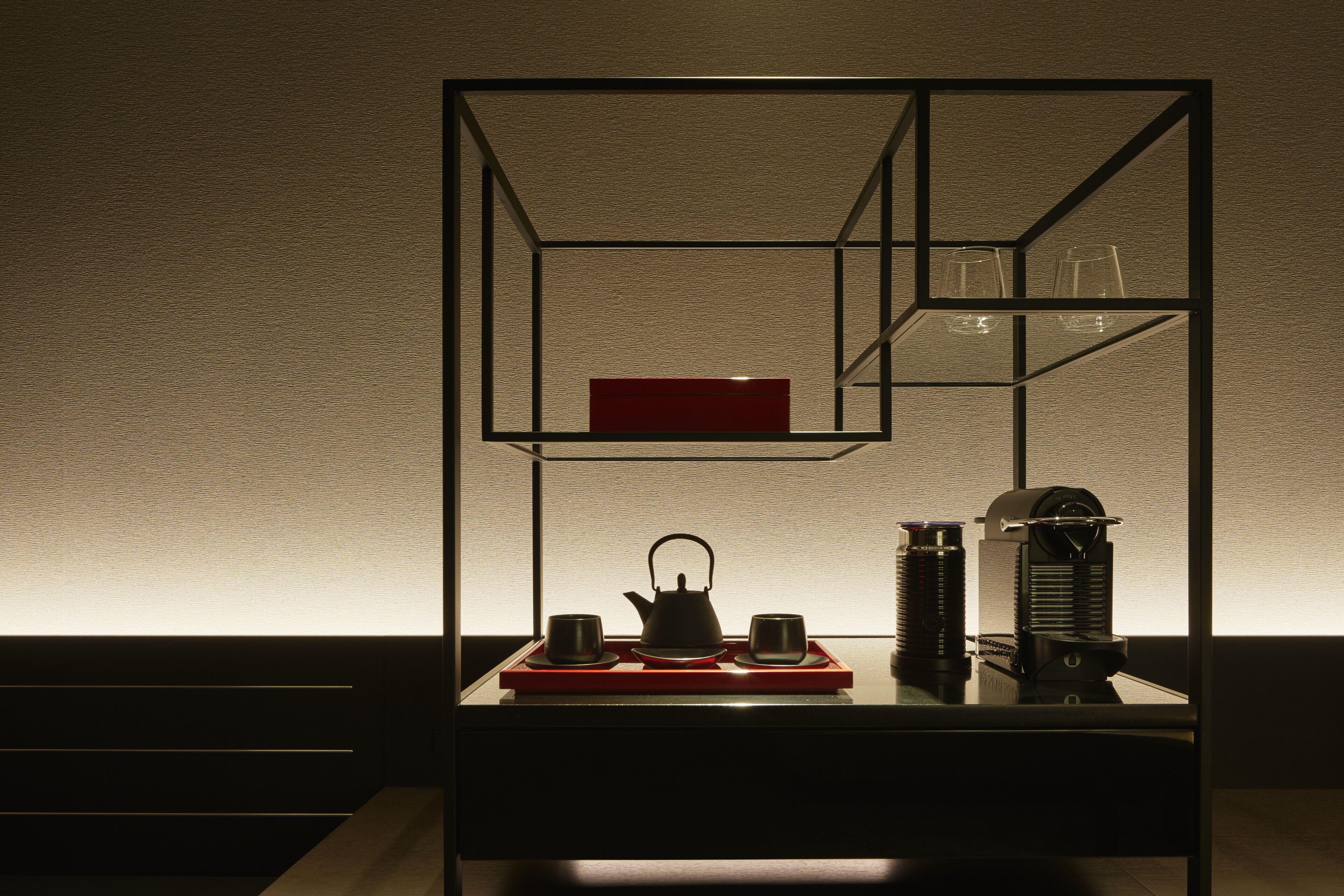 A modern interior with a geometric shelving unit displaying a kettle, cups, and a red box.