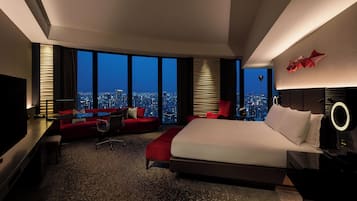 Une chambre d’hôtel moderne avec un grand lit, un canapé rouge, un bureau et une vue sur le paysage urbain.