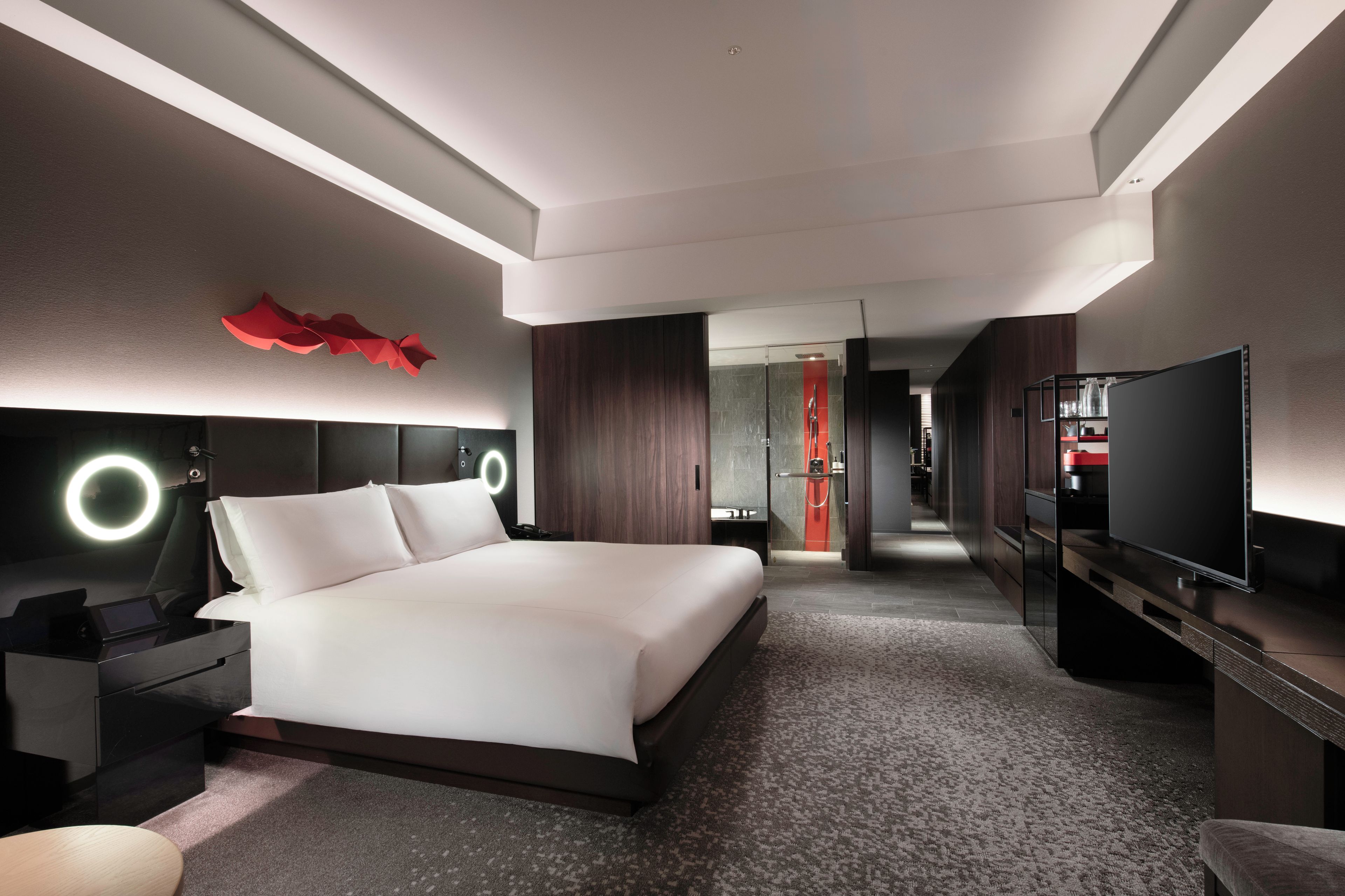 A modern hotel room with a large bed, a TV, a desk, and a bathroom visible through an open door.