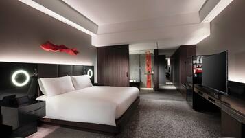 A modern hotel room with a large bed, a TV, a desk, and a bathroom visible through an open door.
