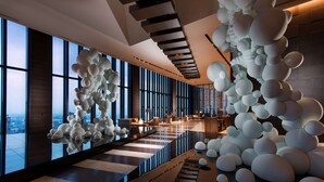 Een moderne hotellobby met een spiegelende vloer, grote ramen met uitzicht over de stad, en een unieke sculptuurinstallatie in de vorm van een bol.