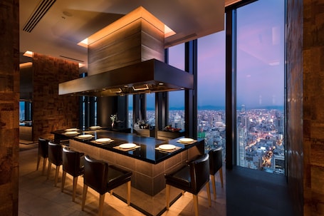 A modern kitchen with a large island, bar stools, and a city view through large windows.