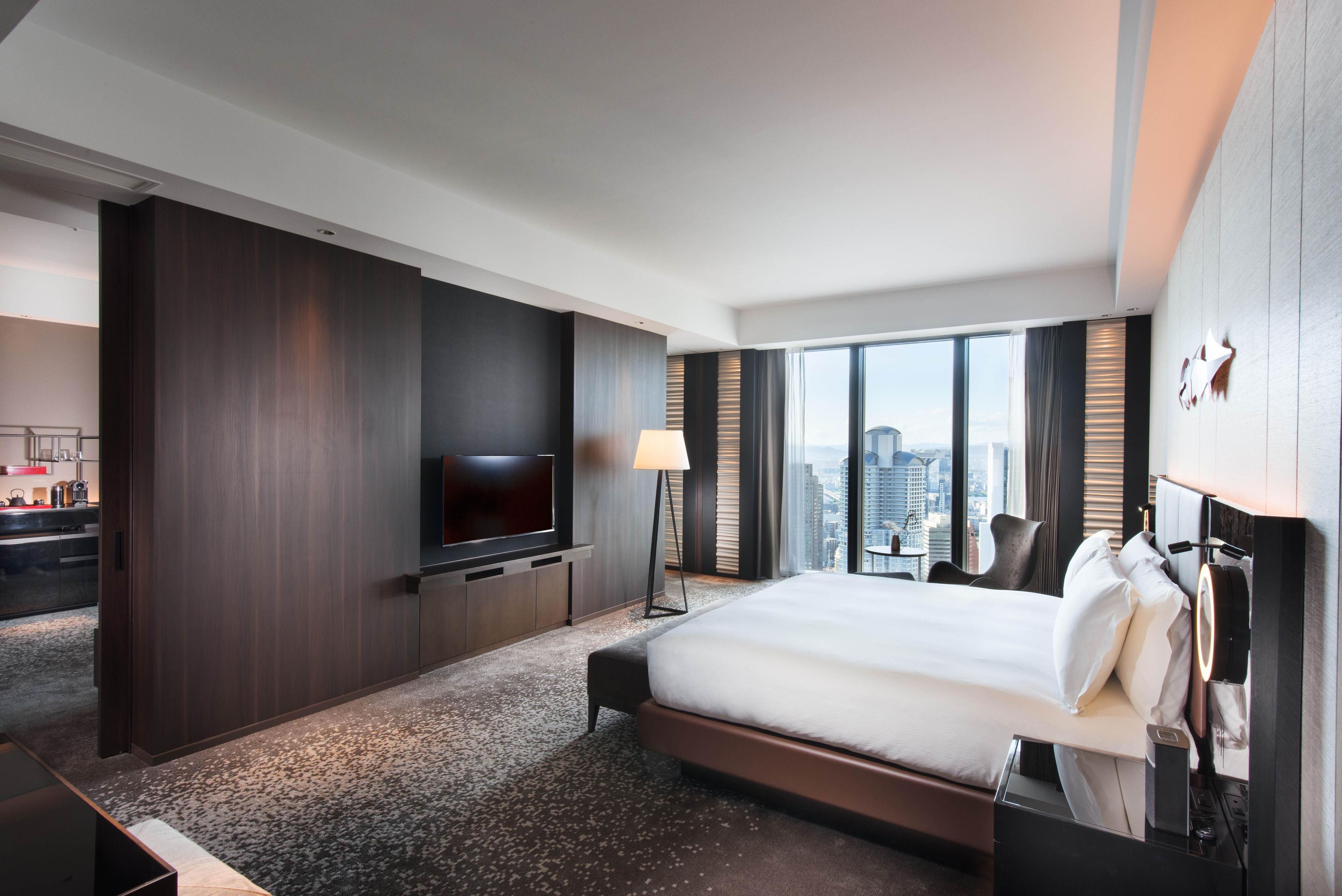 A modern hotel room with a large bed, a flat-screen TV, a desk, and a city view.