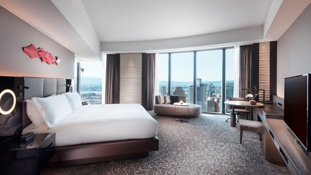 Une chambre d’hôtel moderne, dotée d’un grand lit, d’un bureau, d’une chaise et d’une télévision. La chambre offre une vue sur la ville.