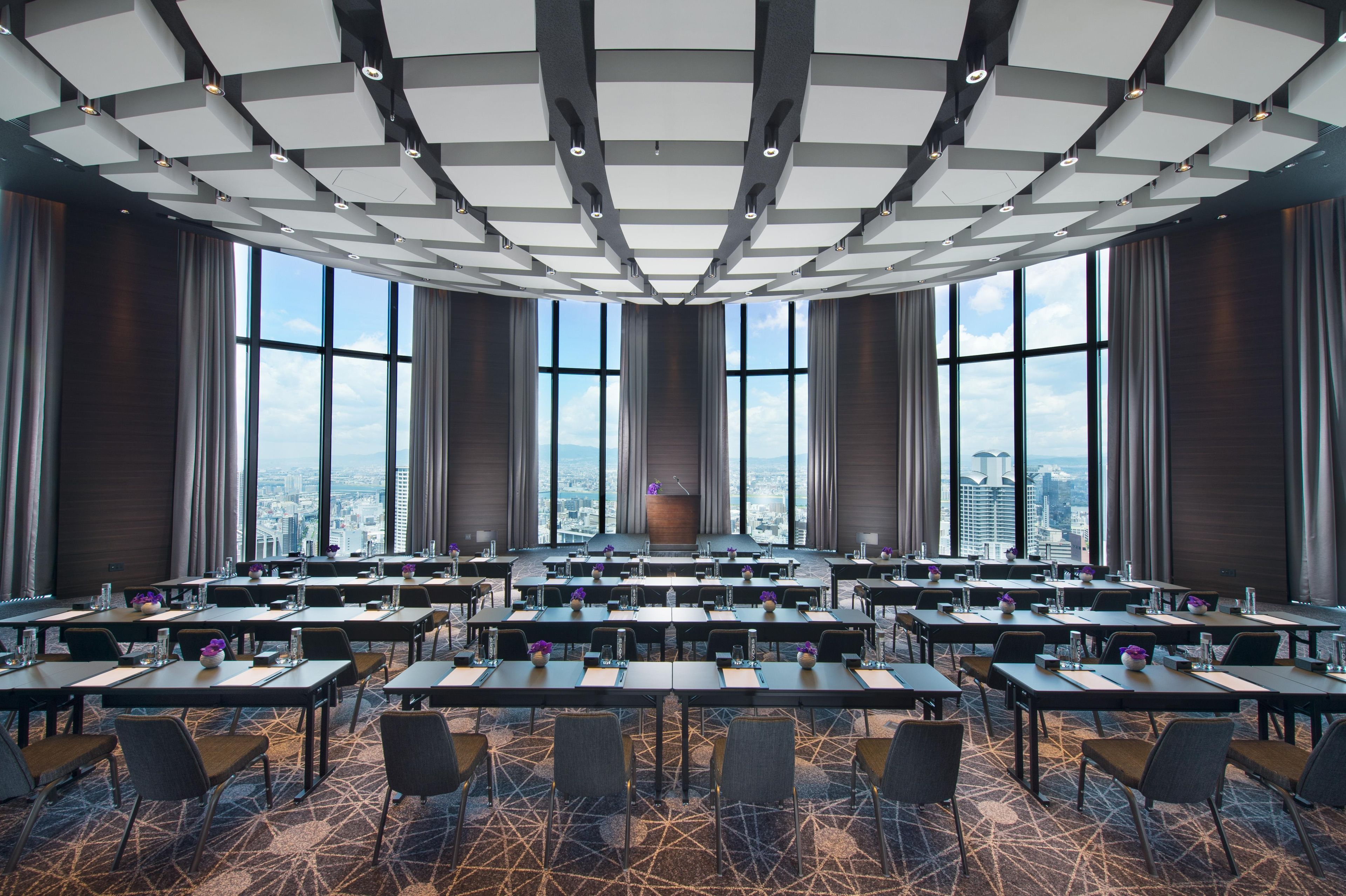 A conference room with a panoramic city view, multiple tables, and a modern ceiling design.