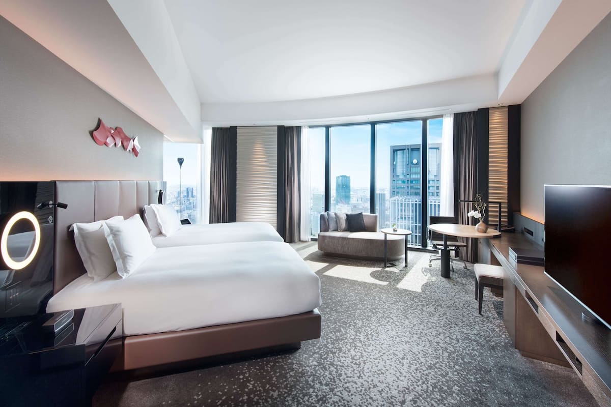 A modern hotel room with a large bed, a desk, a chair, and a TV.