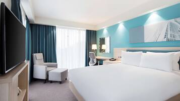 Une chambre d’hôtel avec un grand lit, un téléviseur à écran plat, un bureau avec une lampe, une chaise et une fenêtre avec des rideaux.