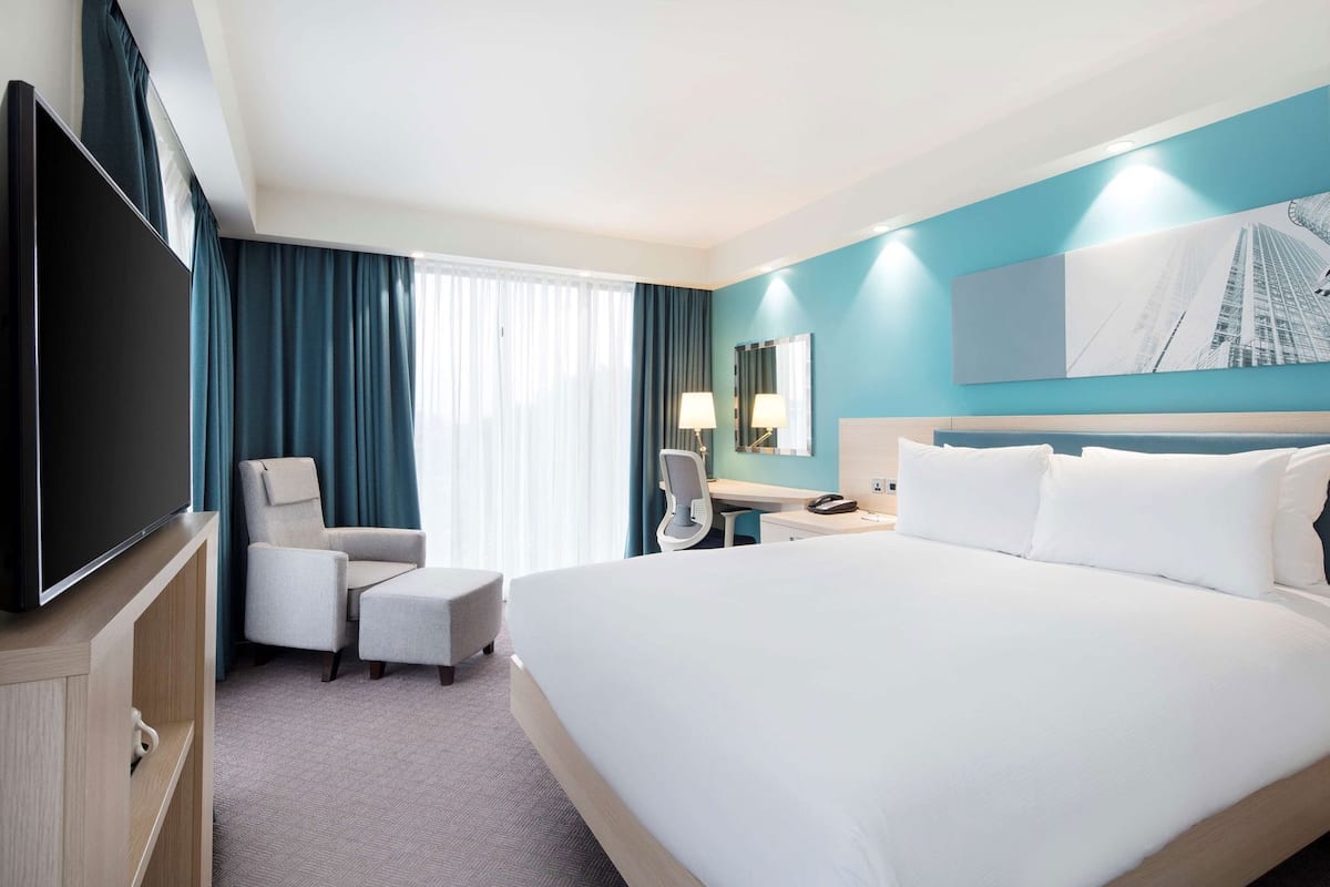 A hotel room with a large bed, a desk with a chair, a television, and a window with curtains.