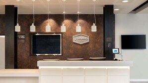 Una moderna reception con un grande schermo, una segnaletica che indica "Hampton by Hilton" e un televisore a schermo piatto sopra.