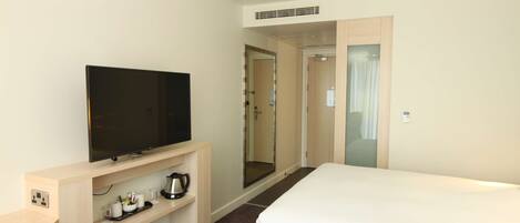 A hotel room with a bed, a TV on a stand, a coffee maker, and a mirror.