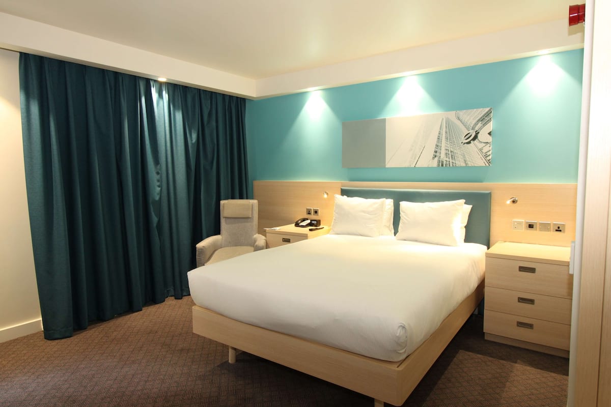 A hotel room with a large bed, a desk, a chair, a nightstand, and a painting on the wall.