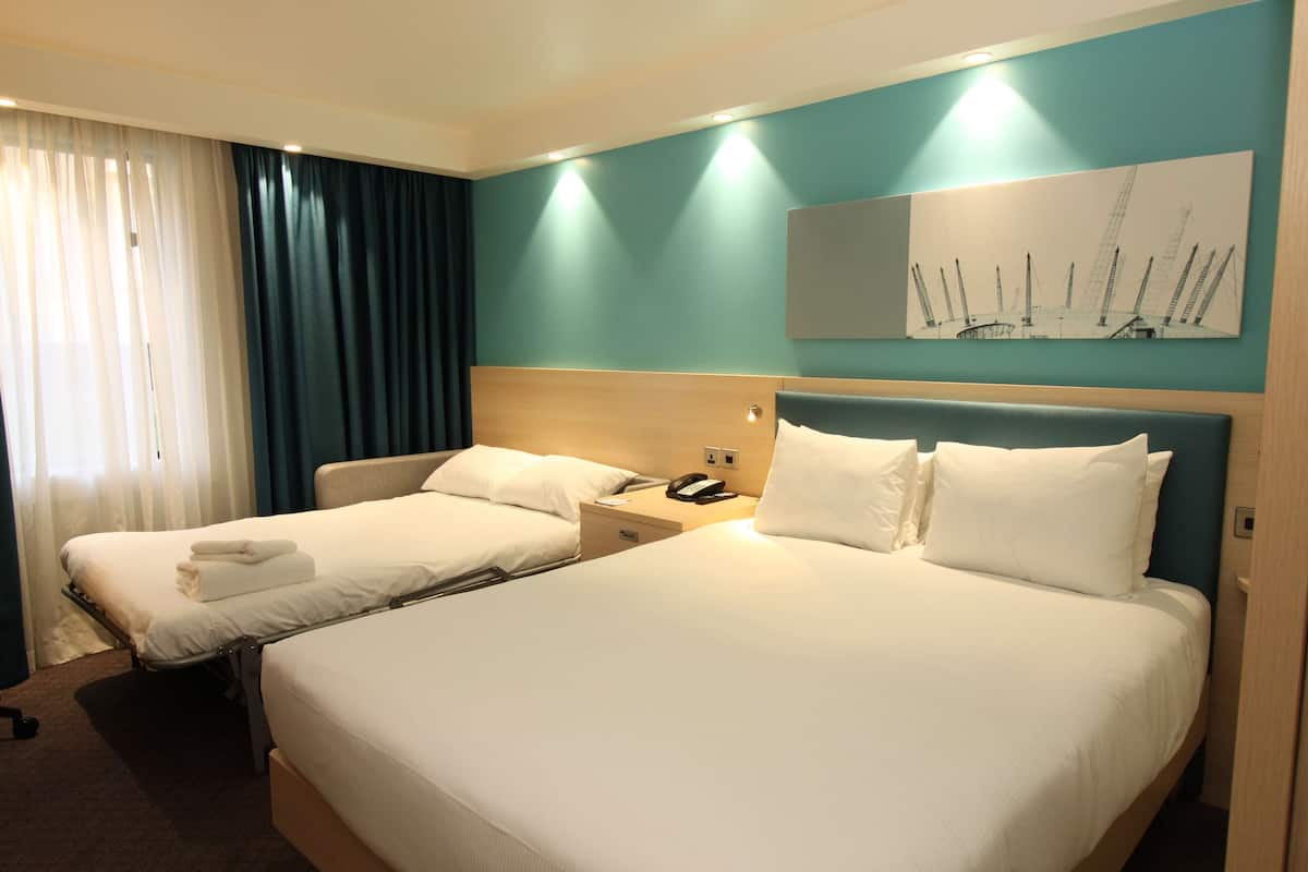 A hotel room with two beds, a wooden headboard, a nightstand with a phone, and a painting of sailboats on the wall.
