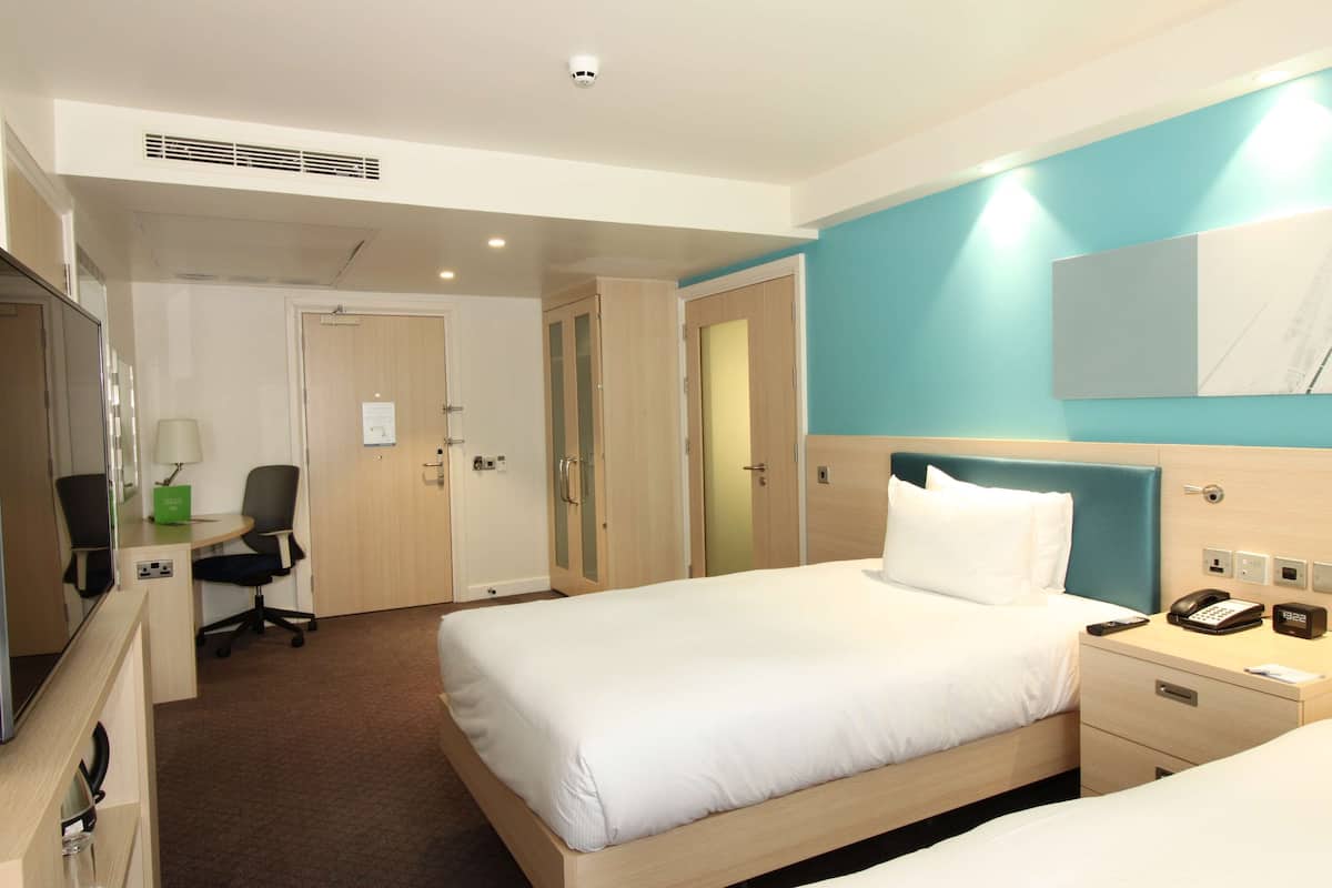 A hotel room with a bed, bedside table, lamp, desk, chair, and a mirror.