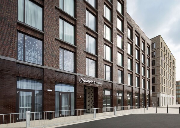 A modern brick building with large windows and a sign that reads "Hampton." - Hampton by Hilton London Excel (London)