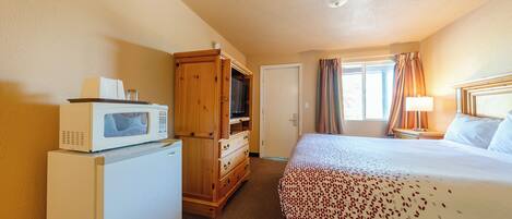 Une chambre d’hôtel avec un lit, un four à micro-ondes, une commode en bois, une porte et une fenêtre avec des rideaux.